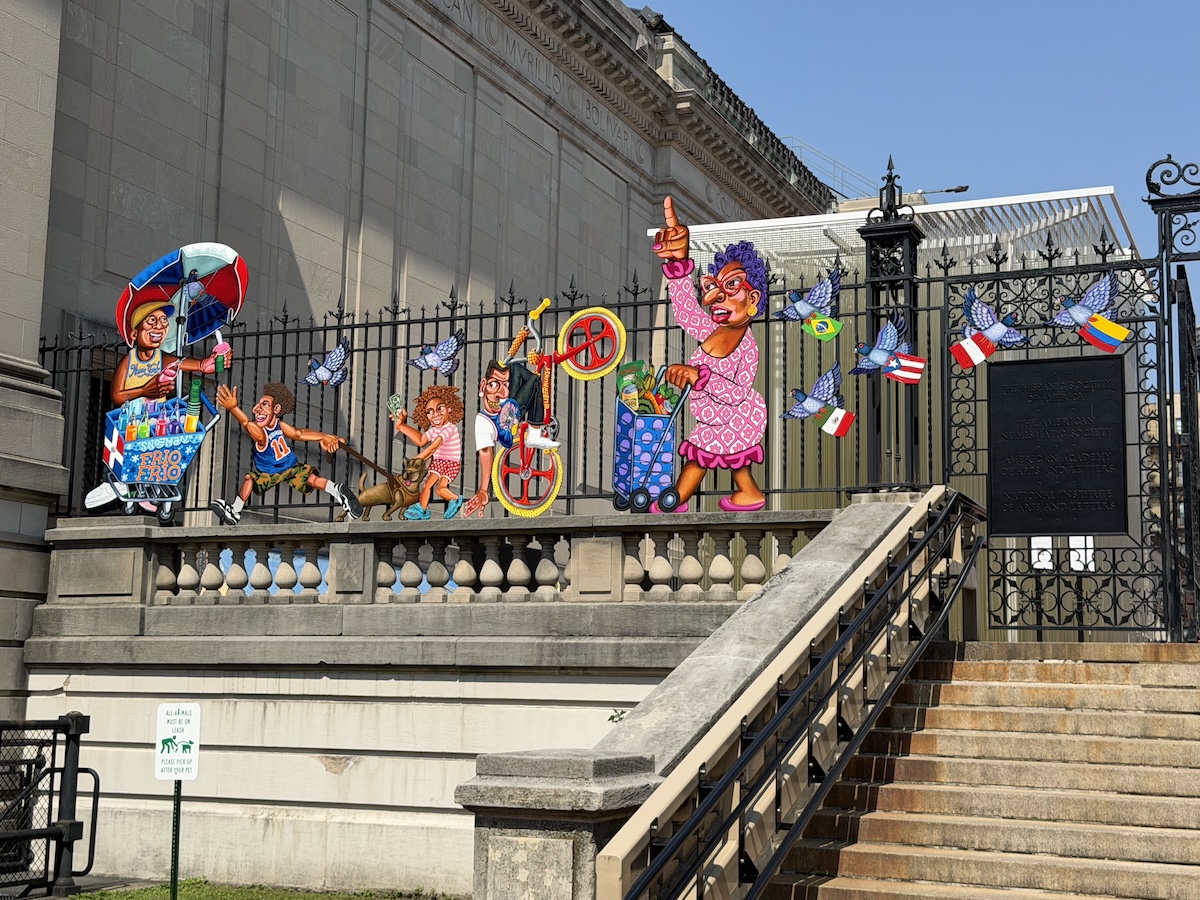 An ornate iron gate with painted cutouts of scenes related to West Harlem and Washington Heights
