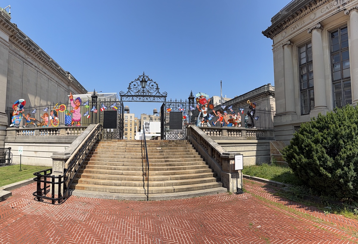 Stairs leading up to the Audubon Terrace, right outside the Hispanic Society Museum and Library. On the left and right hand side is an ornate iron gate with painted cutouts of scenes related to West Harlem and Washington Heights